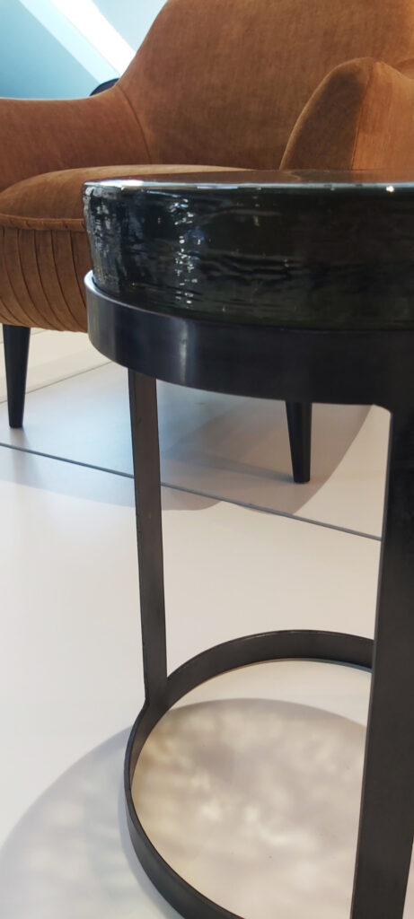 Ein Foto des runden Beistelltisches aus Metall und massiver Glasplatte mit welliger Oberfläche und schlankem Design, der eine perfekte Ergänzung für jeden Raum darstellt.